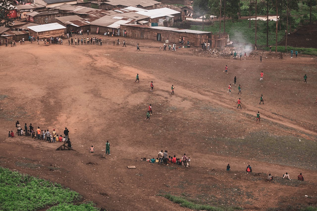 Children play soccer on a rural field while villagers watch. Aerial shot capturing community life.