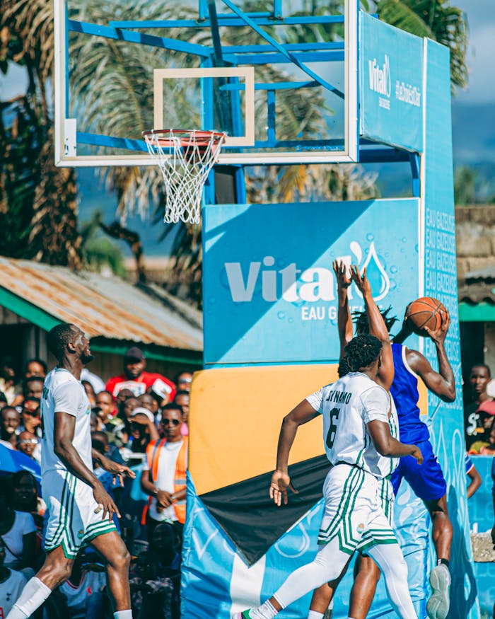 Exciting outdoor street basketball game with intense players in vibrant team jerseys and a lively audience.