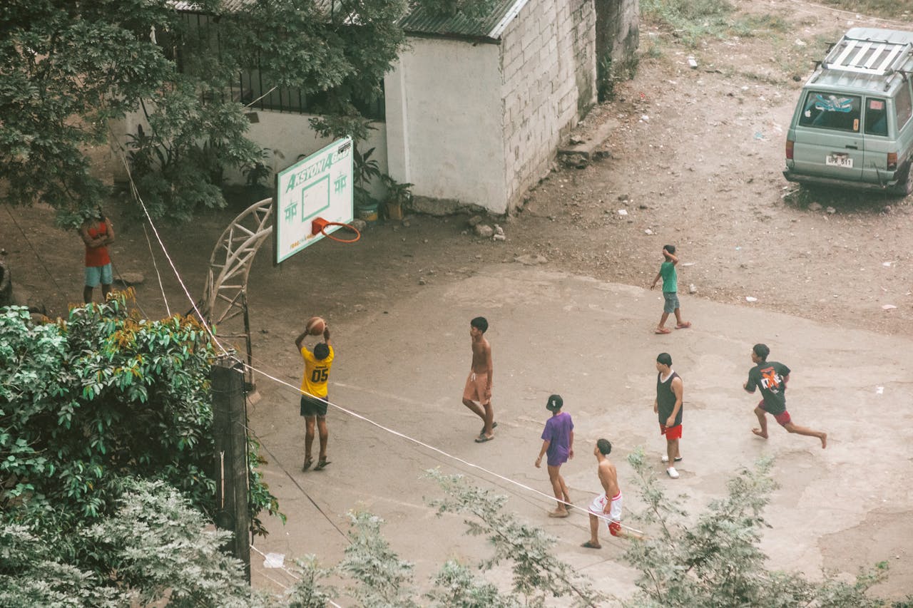 Group of young men playing a casual basketball game on a rural court.