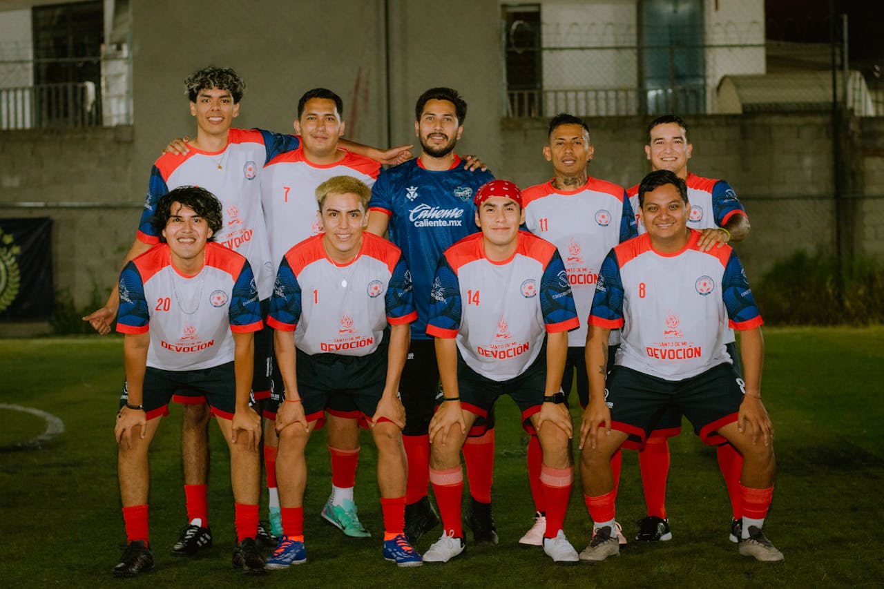 A group shot of an amateur soccer team posing on an outdoor field at night.